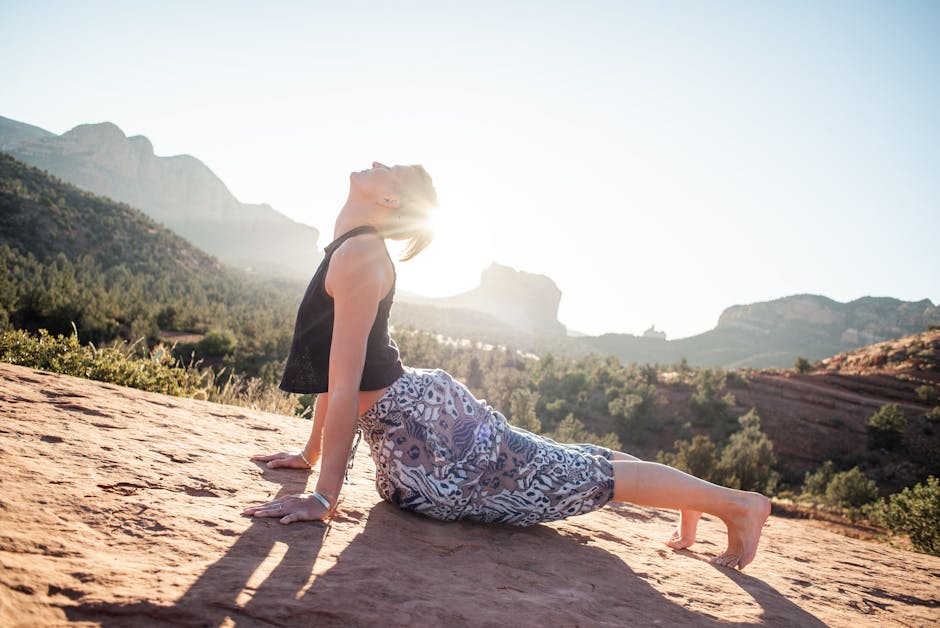 Woman performing a challenging balance yoga pose on a cliff with a serene mountain landscape.